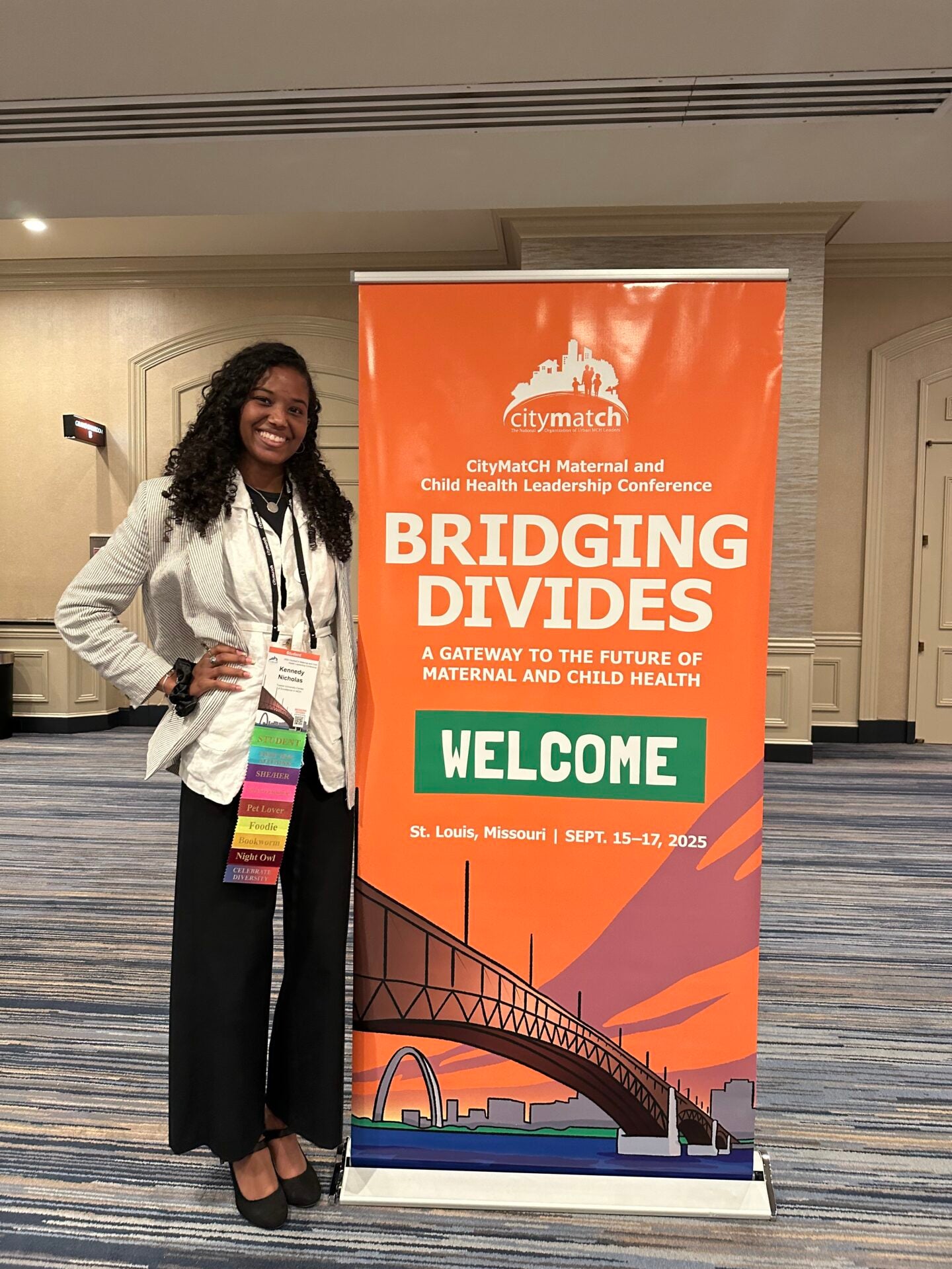Kennedy stands next to an orange poster for the CityMatCH conference 2025.
